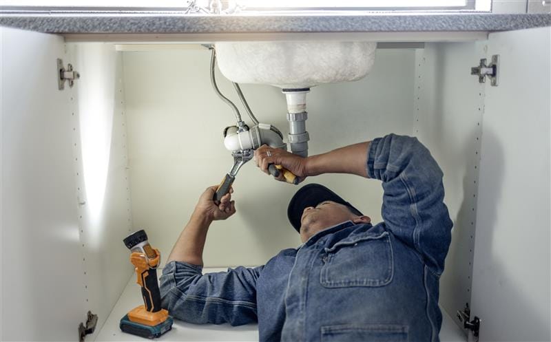 Plumber repairing pipes beneath a bathroom sink in Pittsburgh