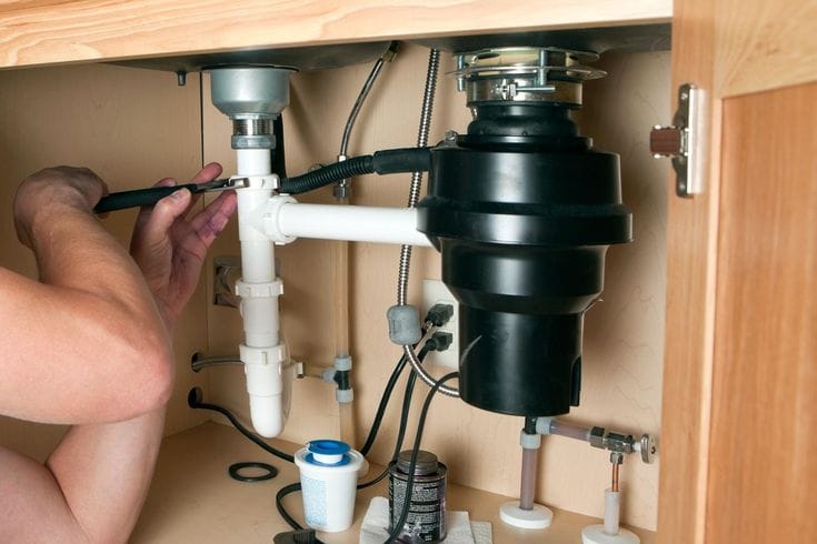 Plumber installing a garbage disposal beneath a kitchen sink in Pittsburgh