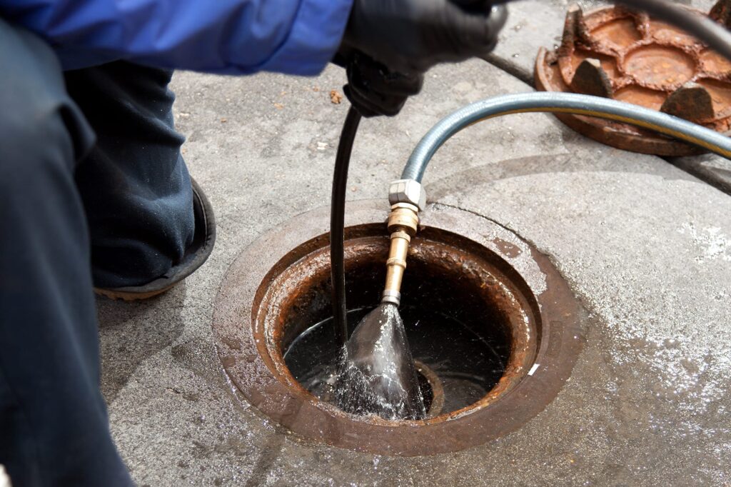 Plumber hydro jetting a sewer line through a manhole in Pittsburgh