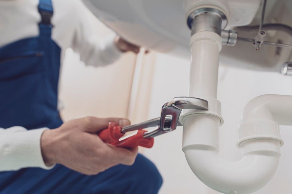 Plumber repairing a white drain pipe beneath a sink in Pittsburgh